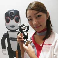 A model shows off Sharp Corp.\'s RoBoHoN, a phone combined with a humanoid robot, at the CEATEC trade fair in the city of Chiba on Tuesday. | KAZUAKI NAGATA