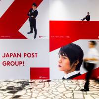 A man walks past a Japan Post Holdings Co. ad at its headquarters in Tokyo in June. | REUTERS
