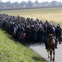 A mounted policeman leads a group of migrants near Dobova, Slovenia, on Tuesday. | REUTERS