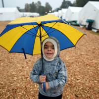 Yazem, a 3-year-old from Aleppo, Syria, holds an umbrella as he stands in front of tents in a refugee camp in Celle, Germany, on Thursday. | REUTERS