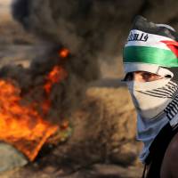A Palestinian protester passes by burning tires during clashes with Israeli troops near the border between Israel and Central Gaza Strip Wednesday. Seven Israelis and 31 Palestinians, including children and assailants, have been killed in two weeks of bloodshed in Israel, Jerusalem and the occupied West Bank. | REUTERS