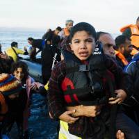 A man carries a boys as they land with other migrants and refugees on the Greek island of Lesbos, after crossing the Aegean sea from Turkey, on Wednesday. More than 400,000 refugees, mostly Syrians and Afghans, arrived in Greece since early January while dozens drowned trying to make the crossing, including a woman and two children Wednesday. | AFP-JIJI