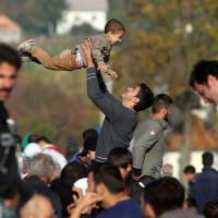 A man plays with a child as migrants and refugees wait in a field on their way to a camp after crossing the Croatian-Slovenian border near Rigonce, Slovenia, on Monday. | AFP-JIJI