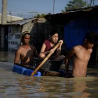 Residents use a raft made of jerry cans to cross a flooded street in Calumpit, Bulacan province, in the Philippines on Thursday. The death toll from Typhoon Koppu climbed to 54 on Thursday, as floods shifted downstream to coastal villages, displacing tens of thousands of residents. | AFP-JIJI