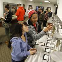 Juliano Hamana (right) and Jayme Jennings (left) browse samples at the Shango Cannabis shop after legal recreational marijuana sales began at midnight in Portland, Oregon, on Oct. 1. | REUTERS