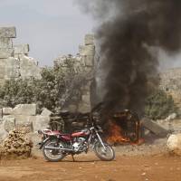 A man runs past a burning military vehicle at a base controlled by rebel fighters from the Ahrar al-Sham Movement that was targeted by what activists said were Russian airstrikes at Hass ancient cemeteries in the southern countryside of Idlib, Syria, Thursday. | REUTERS