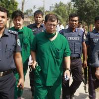 A Japanese doctor (center) and the Japanese Embassy\'s chief security officer (third from left) walk with Bangladesh police as they inspect the body of Kunio Hoshi in Rangpur on Sunday. The Islamic State group claimed responsibility for fatally shooting Hoshi in northern Bangladesh on Saturday, days after they said they were behind the murder of an Italian aid worker in Dhaka. | AFP-JIJI