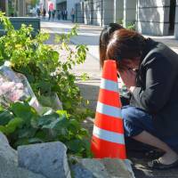 Women pray for the victims of a car crash at the accident site in the city of Miyazaki on Thursday, the day after a minivehicle driven by a 73-year-old man rammed into several pedestrians on a sidewalk, killing two and injuring four. | KYODO