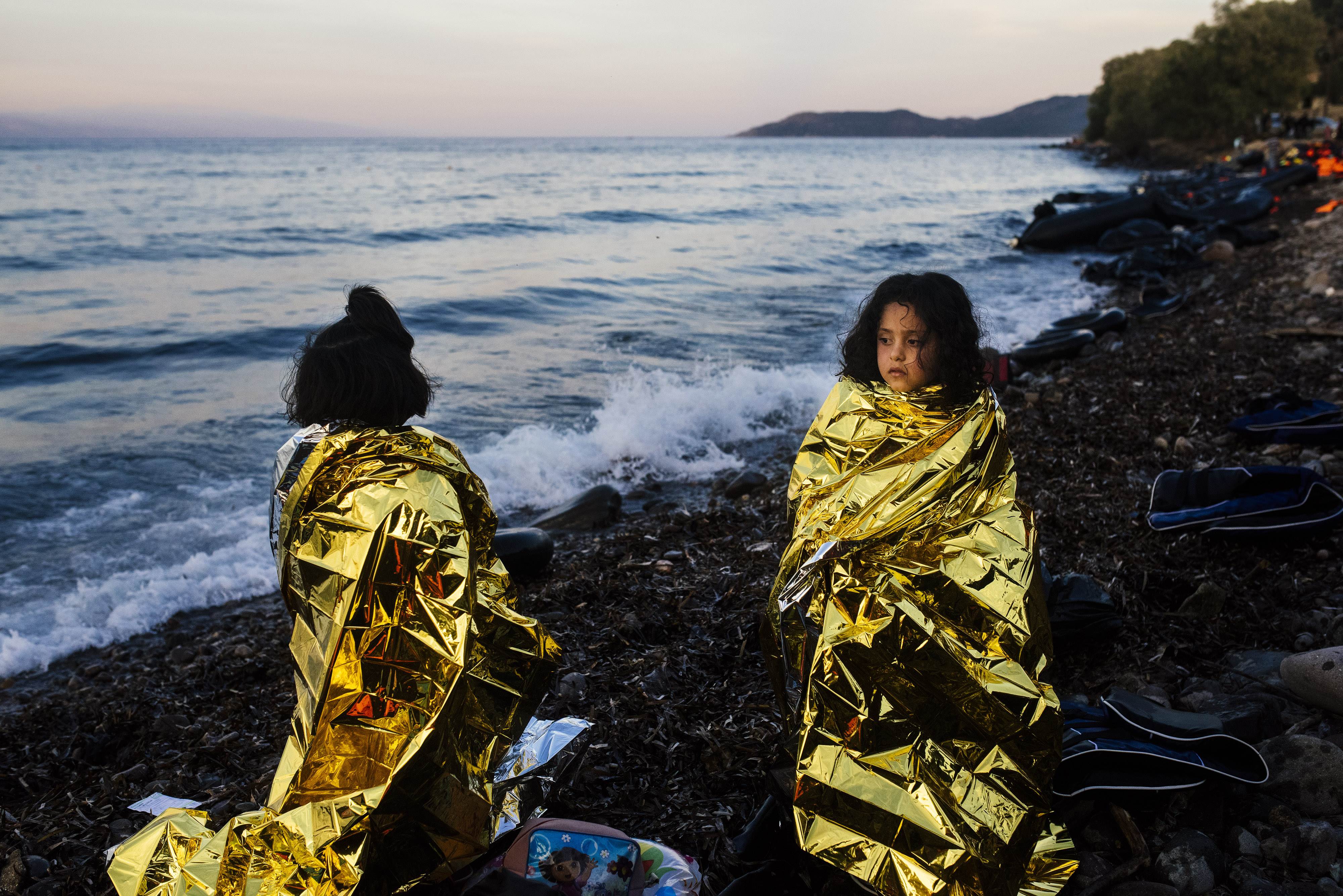 Children stand on a beach wrapped in emergency blankets Wednesday shortly after arriving with other migrants and refugees on the Greek island of Lesbos after crossing the Aegean Sea from Turkey. | AFP-JIJI