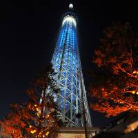 Tokyo Skytree, seen between trees adorned with jack-o\'-lanterns, is illuminated with blue lights Saturday as part of a global celebration to mark the 70th anniversary of the United Nations. | YOSHIAKI MIURA