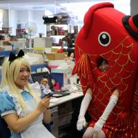 Employees of Japanese toy company Tomy dressed up as characters for Halloween. Pictured are Alice and a large fish wearing a hat seen at their desks during the company\'s Halloween Day event at the company headquarters in Tokyo on Tuesday. | AFP-JIJI