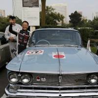 Toyota Motor Corp. President Akio Toyoda holds a torch from the 1964 Tokyo Olympics as he poses with the Prince Gloria DX Official 1964 Tokyo Olympic Car after a parade held Saturday to promote this week\'s Tokyo Motor Show. | REUTERS