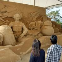 Visitors admire a large sand sculpture featuring characters from the \"Star Wars\" movies in the parking lot at Tottori sand dunes in Tottori Prefecture on Thursday. The 3.4-meter-high by 7.4-meter-wide sculpture, unveiled the same day, will be on display until the end of December, when the latest film in the space fantasy saga is set to be released. | KYODO