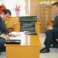 Hakubun Shimomura signs a document handing the portfolio of education and sports minister to newly appointed Hiroshi Hase at the ministry building in Tokyo on Thursday. Shimomura offered to resign following the new stadium debacle. | KYODO