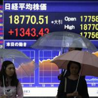 Pedestrians wait to cross a road in front of an electronic display giving the closing figure of the Nikkei stock index outside a securities firm in Tokyo in September. | BLOOMBERG