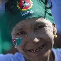 A Myanmar woman wearing traditional \"thanaka\" paste and stickers of the ruling army-backed Union Solidarity and Development Party attends a campaign rally in Mawbi, outside of Yangon, on Tuesday. | AFP-JIJI