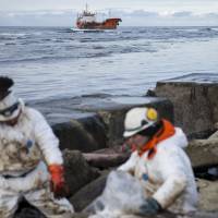 Clean-up workers shovel oil into bags on Russia\'s Sakhalin Island on Sunday. The tanker is seen to the rear. | REUTERS