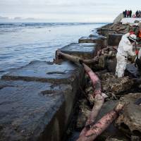 Workers scrape crude oil from the shore in a clean-up effort involving several Russian agencies. The tanker continues to lie on rocks about 150 meters offshore. | AP