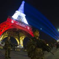 Soldiers stand guard in front of the Eiffel Tower in Paris on Wednesday. The landmark was illuminated in the colors of the French national flag as a tribute to the victims of the Nov. 13 terrorist attacks in the French capital. | AFP-JIJI