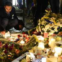 A man lights candles at a makeshift memorial next to the Bataclan concert hall on Monday in Paris. | AFP-JIJI