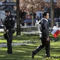 A law enforcement officer stands guard as a man holding a French flag arrives for a tribute to the Paris attacks at the National September 11 Memorial in Manhattan, New York, Monday. | REUTERS