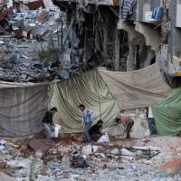 Rebel fighters dig and fill sandbags for barricades behind a sniper curtain to protect them from government forces in the southern Syrian city of Daraa on Wednesday. | AFP-JIJI
