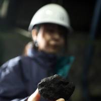 A worker holds up a lump of coal inside a storage yard at the Joban Joint Power Co. Nakoso coal-fired power station in Iwaki, Fukushima Prefecture, in 2012. | BLOOMBERG