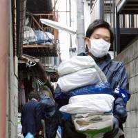 A Kyoto municipal official carries out trash from a so-called garbage house on Friday. | KYODO