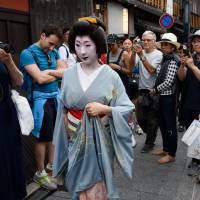 Tourists take photos of a geisha walking through the Gion area of Kyoto in May. | BLOOMBERG