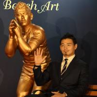 Rugby World Cup hero Ayumu Goromaru sits next to a bronze statue depicting him during an unveiling ceremony Monday for Lighting Bench Art, part of a project to light up the Tokyo Station area for Christmas. It features 11 benches next to sculptures of other famous Japanese, including figure skater Yuzuru Hanyu. | SATOKO KAWASAKI