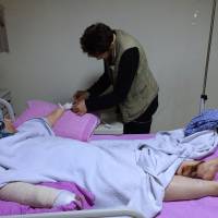 Abdulhamid Khanfoura helps his mother, Zahra, who was burned when her house in the central Syrian village of Habeet was hit during a Russian airstrike, in her hospital bed in the southern Turkish city of Kadirli on Oct. 24. | AP