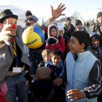A member of Red Noses Clowndoctors entertains migrants before their departure to Austria at a registration center in Dobova, Slovenia, Sunday. | REUTERS