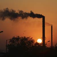The sun sets behind a factory chimney emitting smoke in Ahmadabad, India. | AP