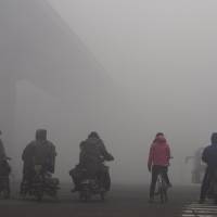 Residents on their bicycles and electric bikes wait at an intersection amid heavy smog in Shijiazhuang, Hebei province, China. | REUTERS