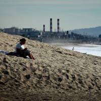 A woman sits on a sand berm created by city workers to protect houses from El Nino storms and high tides at Playa Del Rey beach in Los Angeles on Monday, the day of the start of the U.N. climate conference in Paris. | AFP-JIJI