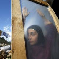 A Syrian refugee stands behind a door at a makeshift settlement in the village of Ketermaya, south of Beirut, earlier this year. | REUTERS