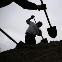 Volunteers use shovels atop a pile of sand as they help fill sandbags Tuesday in St. Louis. Flooding across Missouri has forced the closure of hundreds of roads and threatened homes. | AP