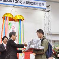 Kiyoshi Ejima, parliamentary vice minister of tourism, presents gifts to a Chinese family at the port of Fukuoka on Wednesday to celebrate attracting 1 million cruise ship visitors from abroad this year. | KYODO
