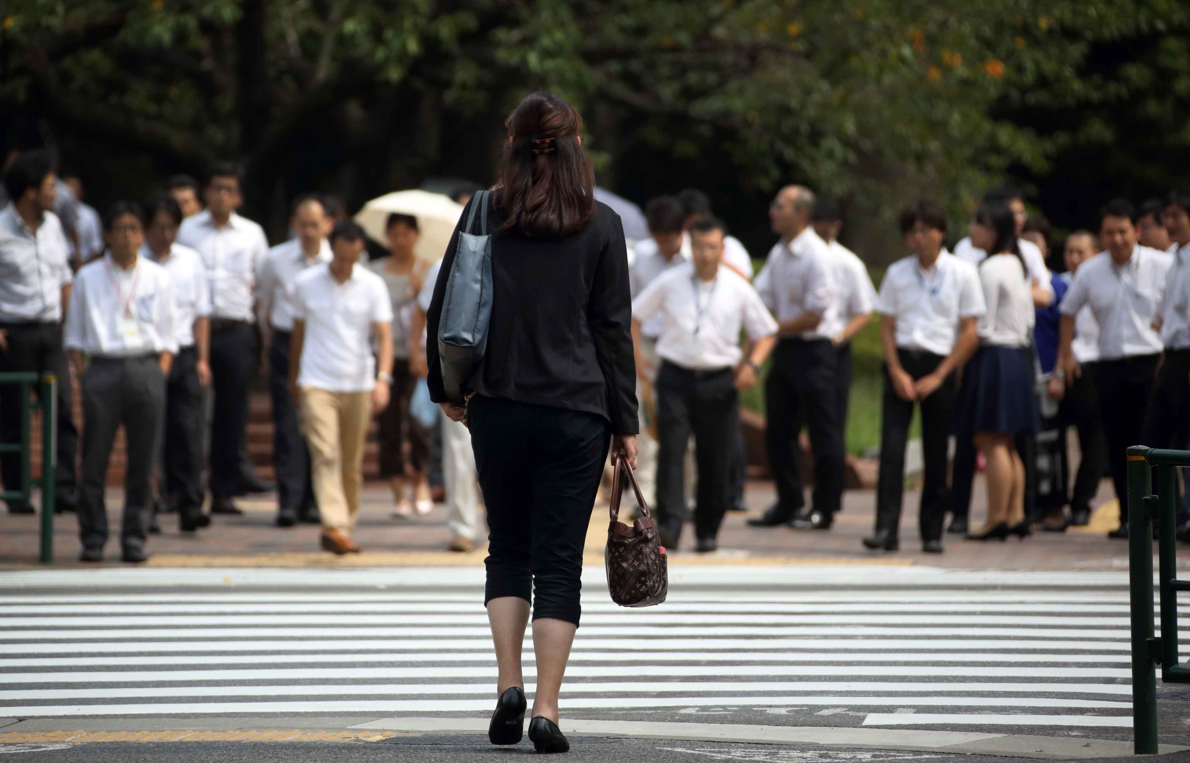 A lone woman waits to cross a street in Tokyo. A government advisory panel on gender equality submitted a report Tuesday urging the nation to change the male-oriented work culture. | BLOOMBERG