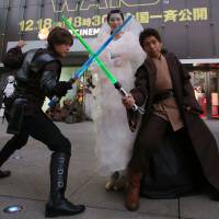 Men wielding lightsabers strike a pose with a woman dressed as Padme Amidala in front of Toho Cinemas\' Roppongi Hills theater in Tokyo\'s Minato Ward on Friday ahead of the premiere of \"Star Wars: The Force Awakens.\" | RIE ISHII