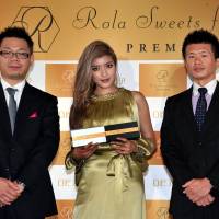 Model and TV personality Rola (center) holds \"Rola Sweets factory PREMIUM\" gateau chocolat and white chocolate cakes during a press conference announcing their release, with collaborating company, ROPIA Ltd., President Eiji Takai (left) and Managing Director Hajime Kawai at Arkangel Daikanyama in Tokyo on Dec. 15. (<a href=\'http://www.rolasweetsfactory.jp\' target=\'_blank\'>www.rolasweetsfactory.jp</a>) | YOSHIAKI MIURA