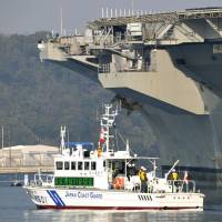 A Japan Coast Guard vessel is dwarfed by the aircraft carrier USS Ronald Reagan at the U.S. naval base in Yokosuka, Kanagawa Prefecture, on Thursday. Officers were taking part in a drill simulating a minor radioactive leak from the nuclear-powered giant, which has been based out of Japan since October. | KYODO