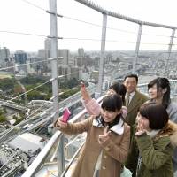 Young women on Friday take pictures from an observation deck that recently opened at the top of Tsutenkaku Tower in the city of Osaka. The 300-meter-tall Abeno Harukas skyscraper, the country\'s tallest building, is seen on the left. | KYODO