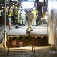 Construction workers check a sidewalk sinkhole in Nagoya on Monday night after a stretch of brick near a construction site about 300 meters from Meitetsu Nagoya Station caved in by about 5 meters. There were no injuries. | KYODO