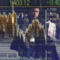 A man is reflected in the electronic board of a securities firm in Tokyo on Friday. | AP