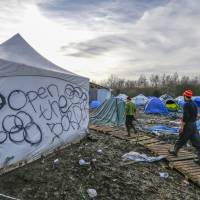 Migrants walk in a muddy field at a camp of makeshift shelters for migrants and asylum-seekers from Iraq, Kurdistan, Iran and Syria, called the Grande Synthe jungle, near Dunkirk, France, Monday. | REUTERS