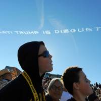 Parade spectators watch as airplane skywriters write a message \"America is great! Trump is disgusting\" above the parade route during the 127th Rose Parade in Pasadena, California, Friday. | AP
