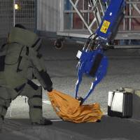 A police officer in protective gear approaches a box suspected of containing an explosive device in a residential area of Ichikawa, Chiba Prefecture, shortly after midnight Saturday. Police later said no explosives were found in it. | KYODO