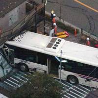 Officials inspect the scene where a bus crashed into an apartment building in Koganei, Tokyo, Thursday. | KYODO