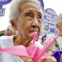 A Filipina survivor of a World War II Japanese military brothel holds a paper crane, a symbol of peace, during a rally in Manila on Wednesday. | KYODO